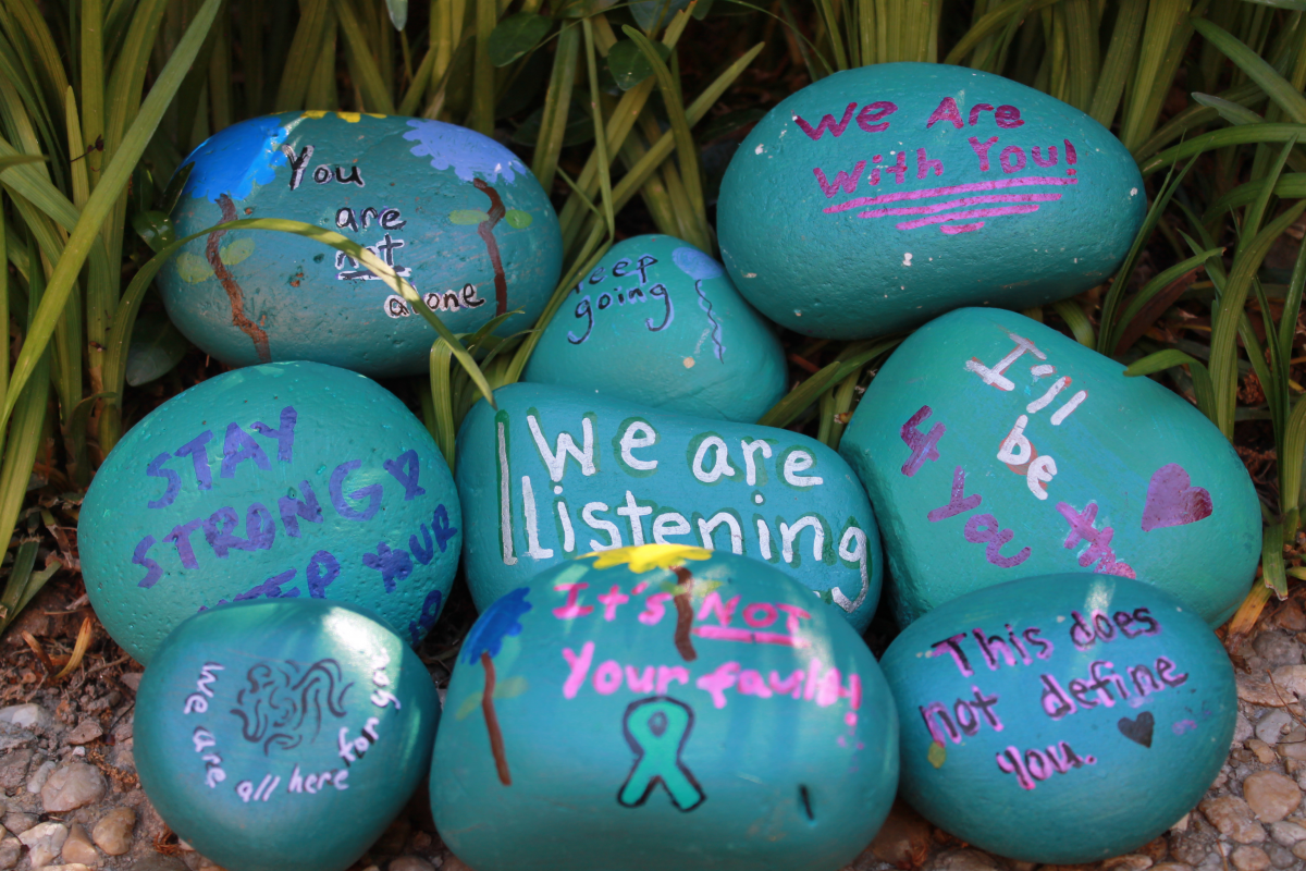 A group of rocks painted teal with written positive messages.